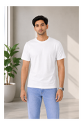 Man wearing a white t-shirt and light blue jeans standing indoors with a plant in the background