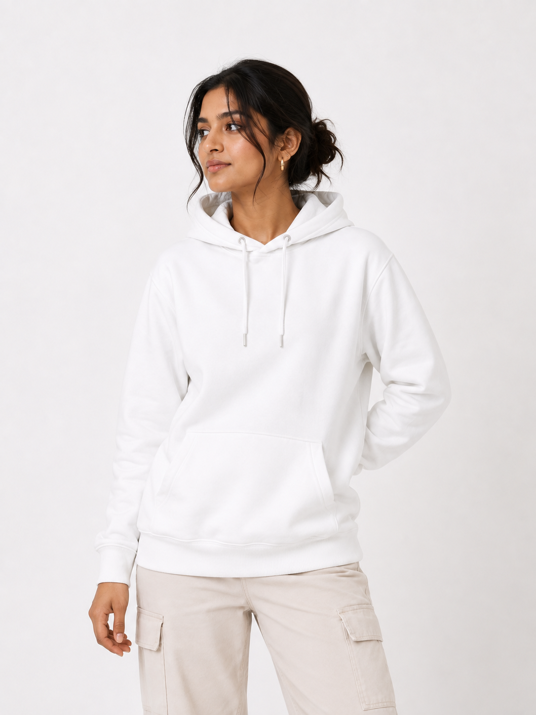 A woman wearing a white pullover hoodie with a front kangaroo pocket and drawstrings, paired with light beige cargo pants, photographed against a clean white studio background.