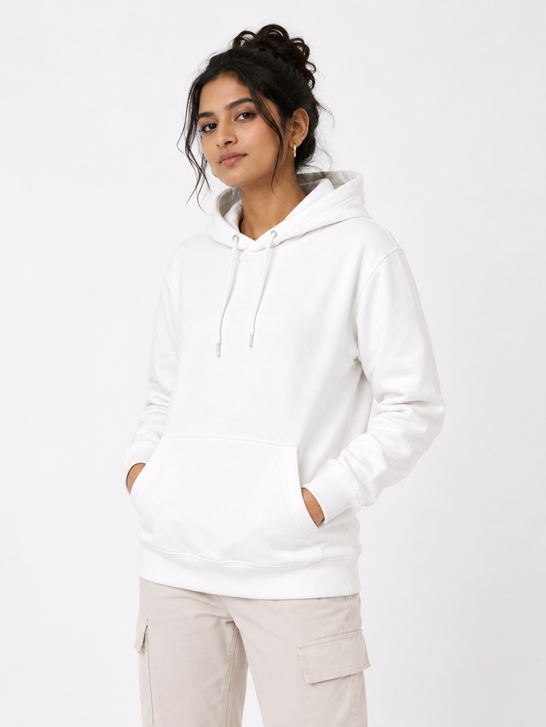 A woman wearing a white pullover hoodie with drawstrings and a front kangaroo pocket, paired with light beige cargo pants, against a plain white studio background.