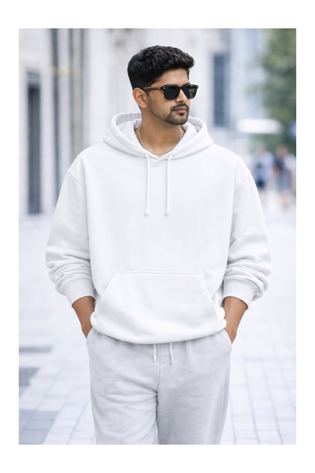Man wearing a white hoodie and light gray pants on a blurred street background