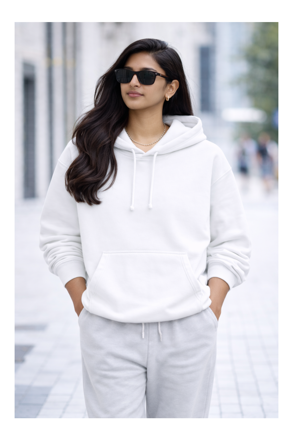 Woman wearing a white hoodie and light gray pants on a blurred street background