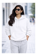 Woman wearing a white hoodie and light gray pants on a blurred street background
