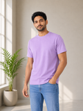 Man wearing a purple t-shirt and blue jeans standing in a bright room with a plant.