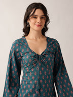 A woman wearing a teal long-sleeve kurta with a pink floral block print and a front tie detail, photographed against a neutral light gray background.