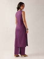 A woman modeling a sleeveless purple kurta with matching wide-leg trousers, shown from a rear three-quarter angle against a plain light beige studio background.