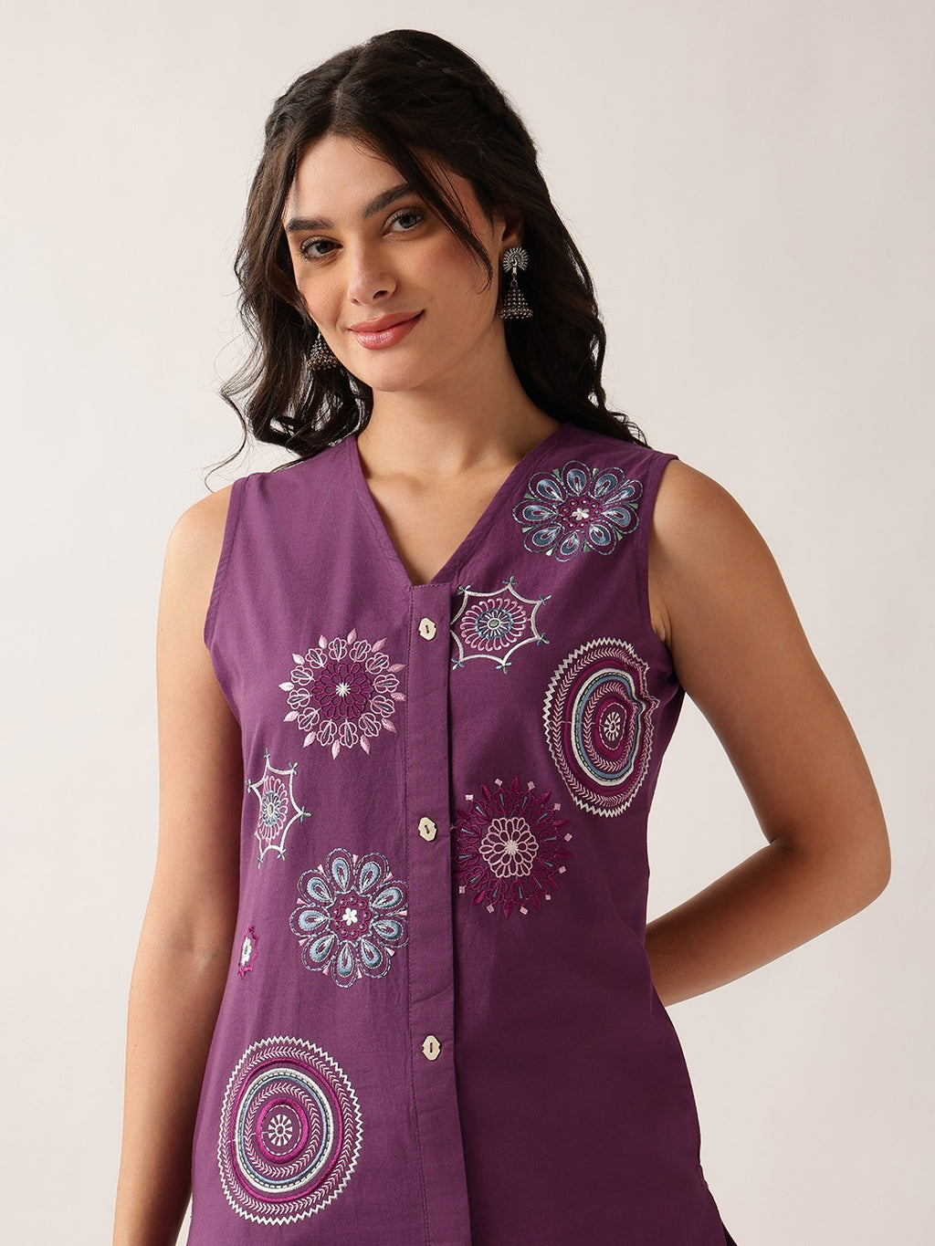 A woman wearing a sleeveless purple button-front top with colorful embroidered mandala patterns, photographed against a plain light background.