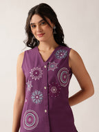 A woman wearing a sleeveless purple button-front top with colorful embroidered mandala patterns, photographed against a plain light background.