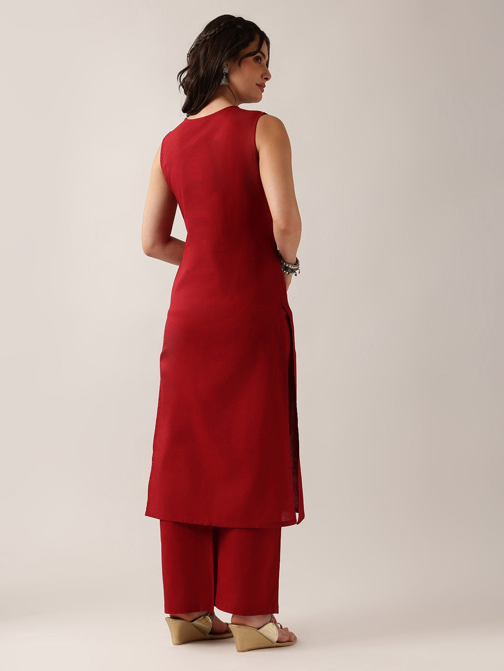 A woman shown from the back wearing a sleeveless red kurta and matching red pants, standing against a plain light beige studio background.