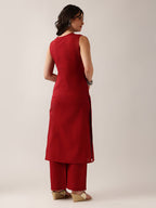 A woman shown from the back wearing a sleeveless red kurta and matching red pants, standing against a plain light beige studio background.
