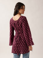 A woman wearing a long-sleeved maroon tunic top with a pinkish floral block print pattern, shown from the back against a plain light background.