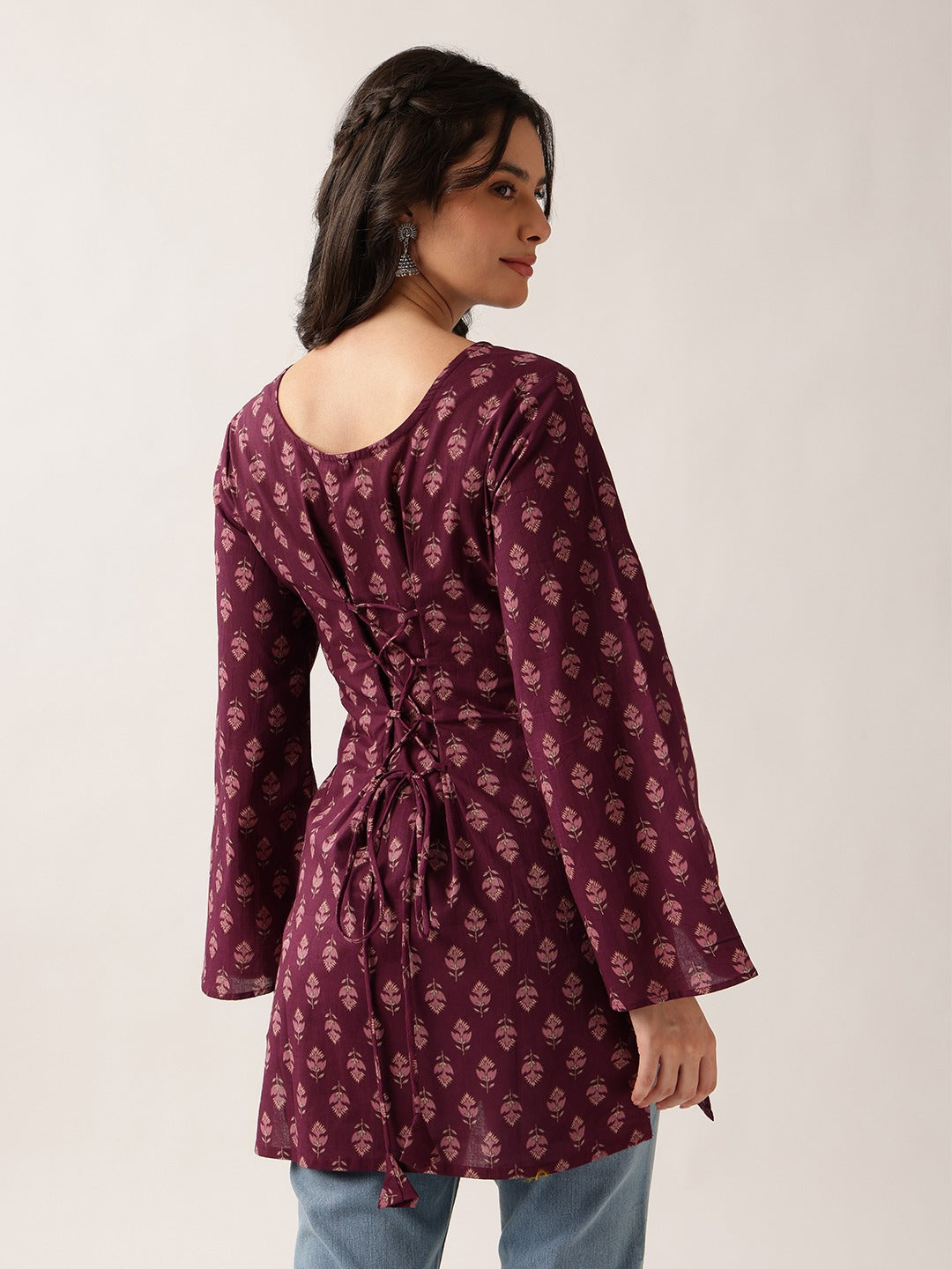 A woman wearing a long-sleeved maroon tunic top with a pinkish floral block print pattern, shown from the back against a plain light background.
